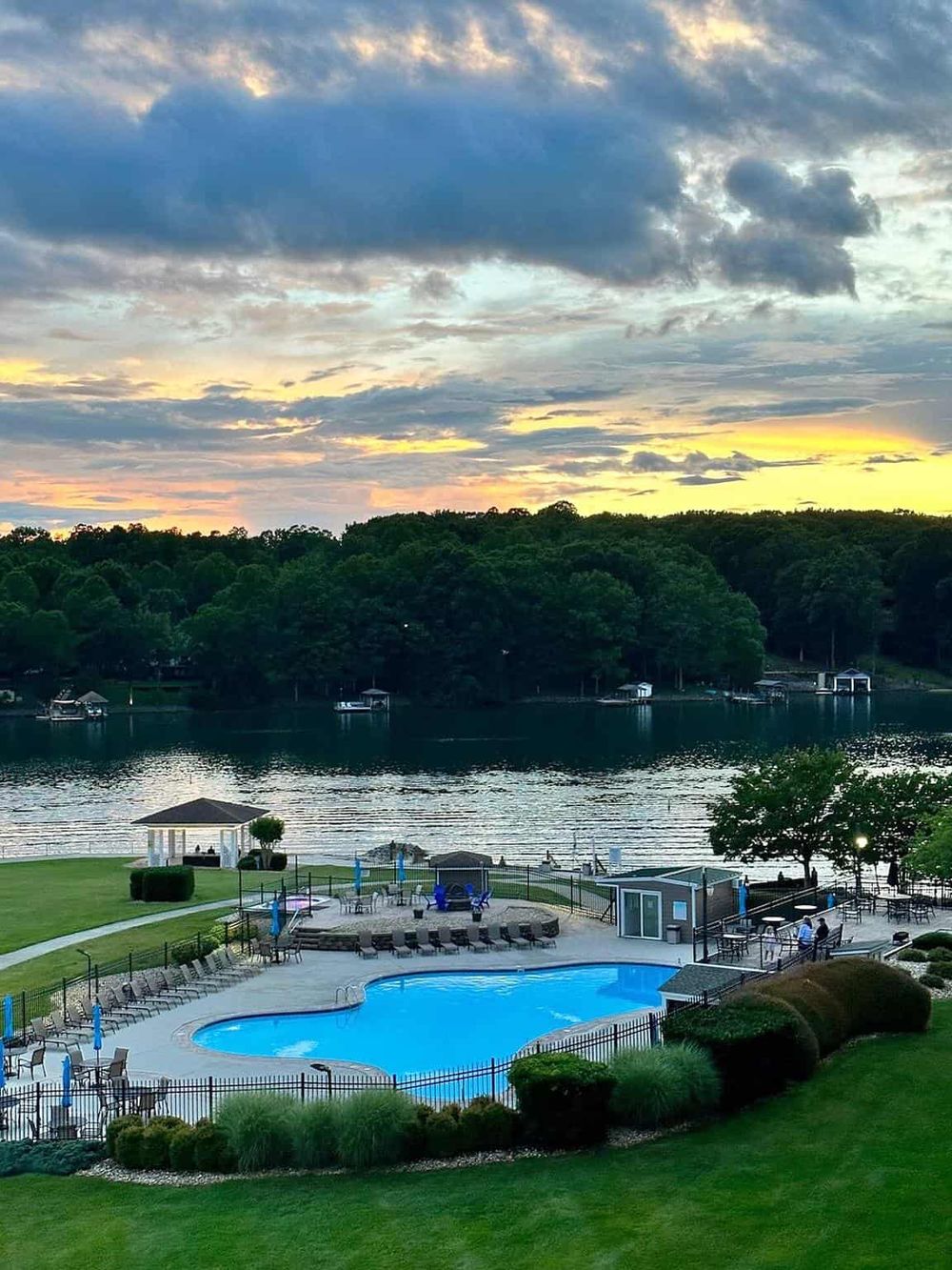 Scenic lakeside pool area at dusk with sunset, boats, and lush greenery at Quest for Directions.