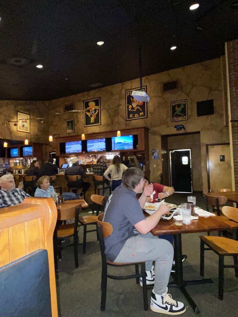 Cozy restaurant interior with patrons enjoying meals and large TV screens, perfect for casual dining and sports viewing.