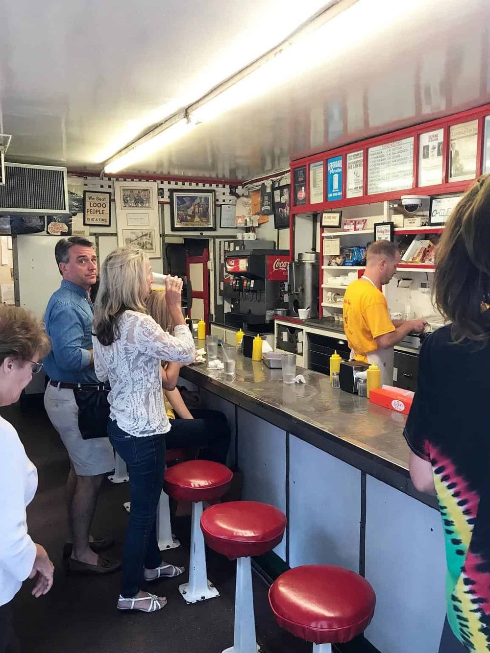 Old-fashioned diner interior with customers ordering food at the counter. Casual dining experience with retro decor and red bar stools.