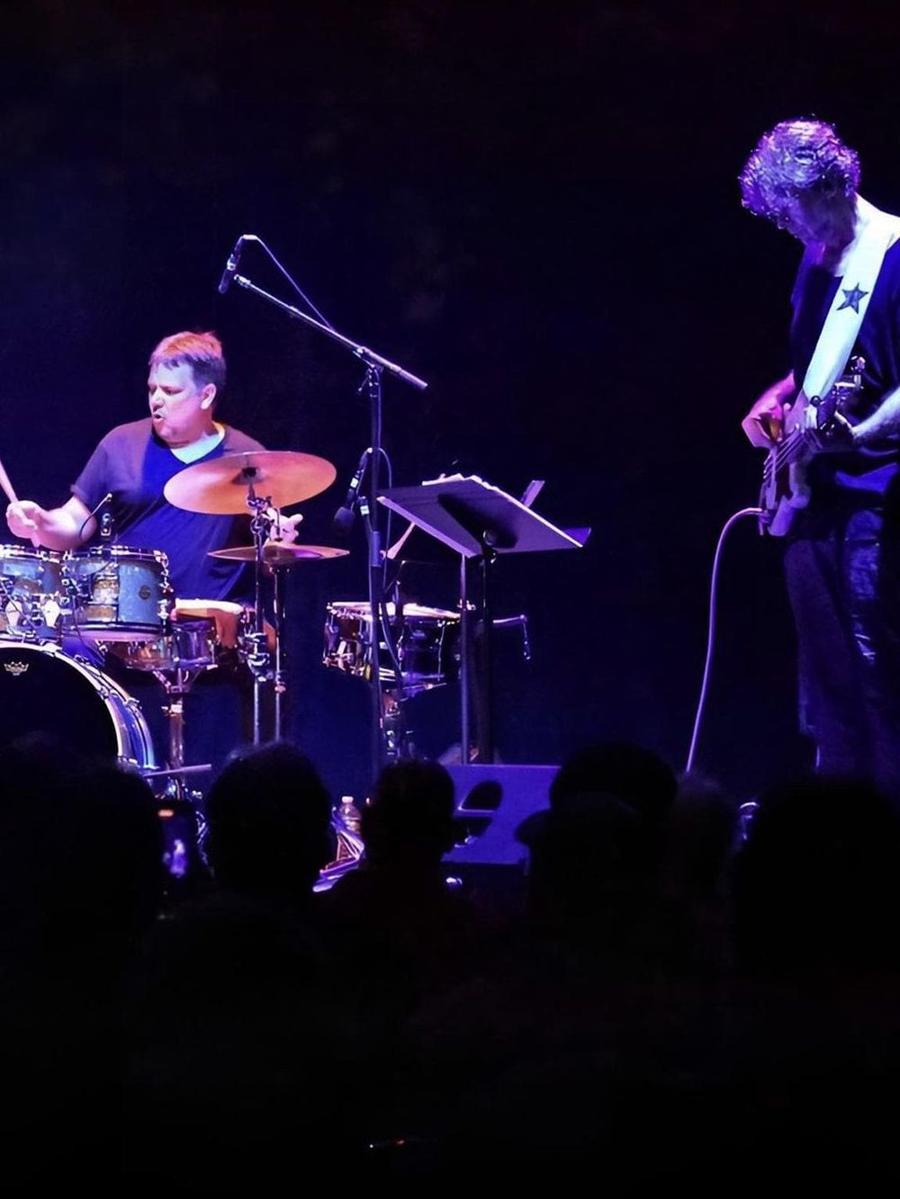 Youth drummer and guitarist performing live on stage at a musical event.