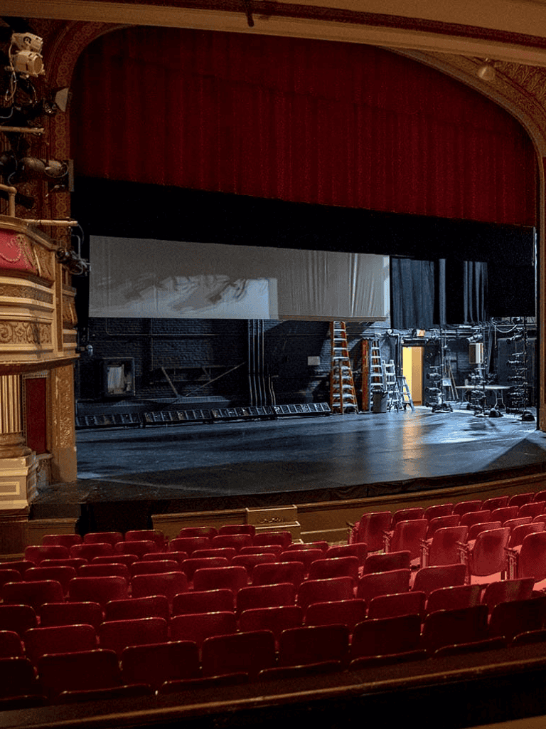 Stage theater with red velvet seats and a large screen, production setup in progress, theater interior for live performances.