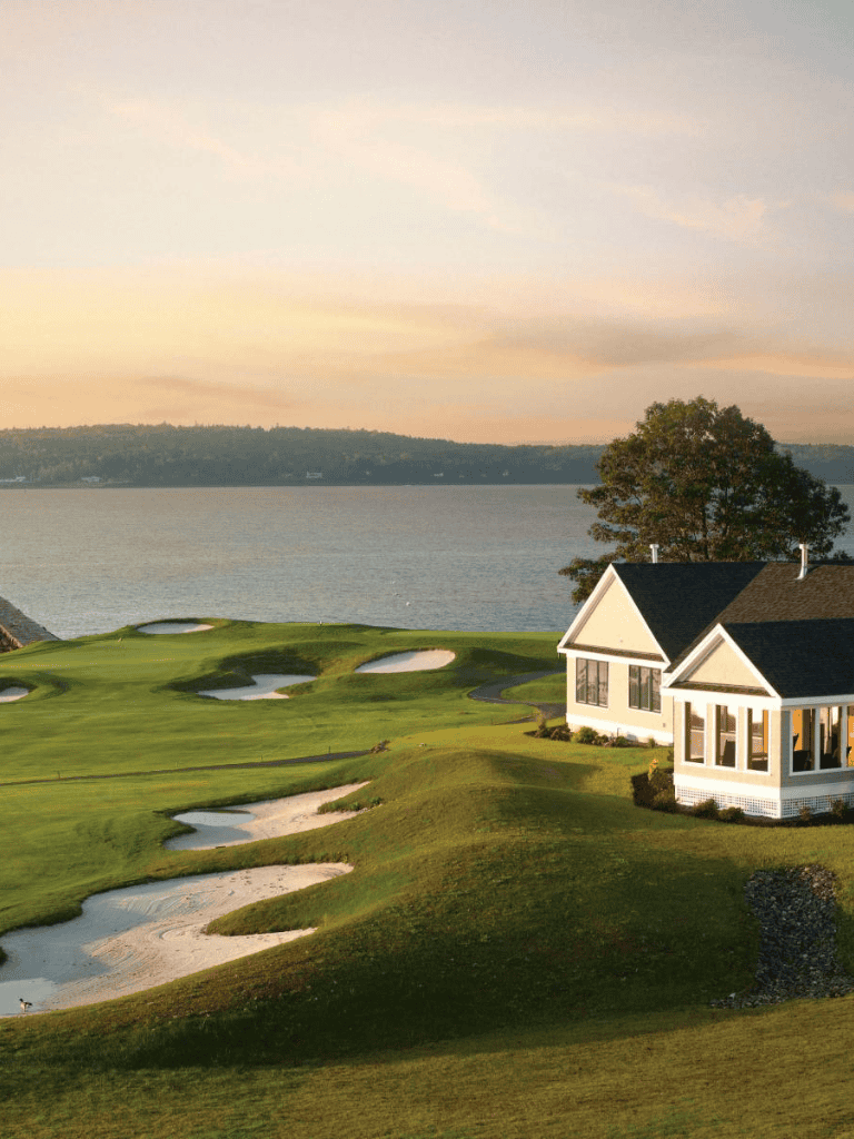 Beautiful golf course with sand bunkers near a lake at sunset, featuring a house with large windows.