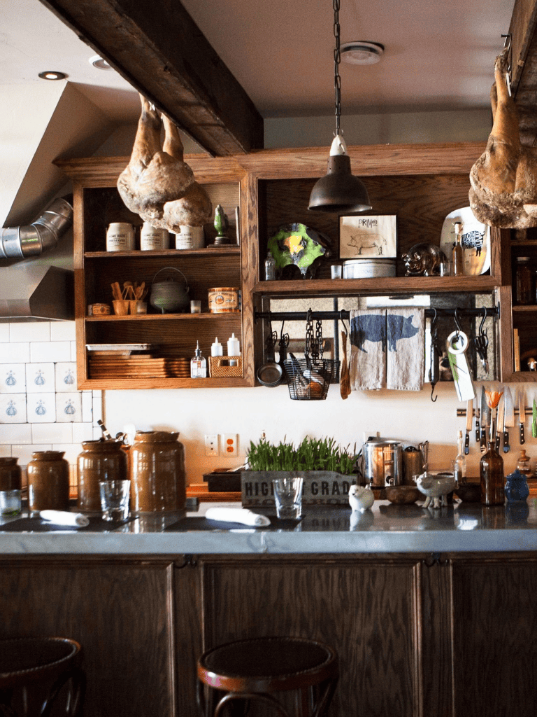 Rustic kitchen with hanging herbal meats, wooden shelves, and farmhouse decor showcasing cozy culinary style.