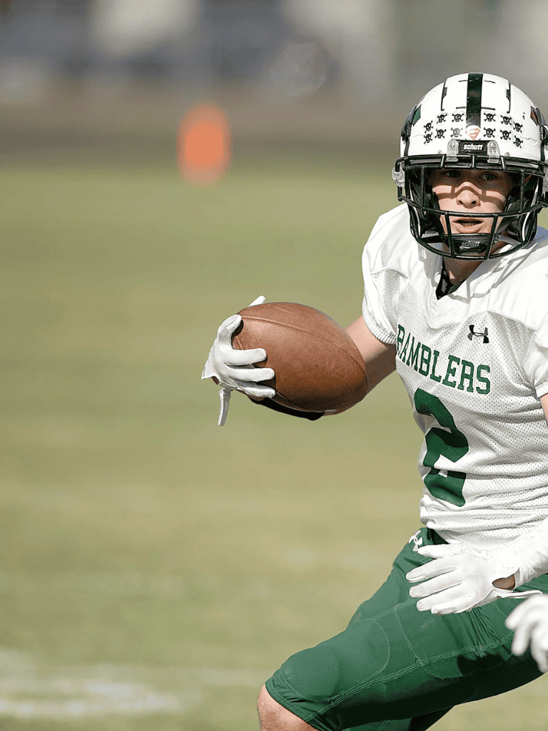 Youth football player in uniform holding football on field.