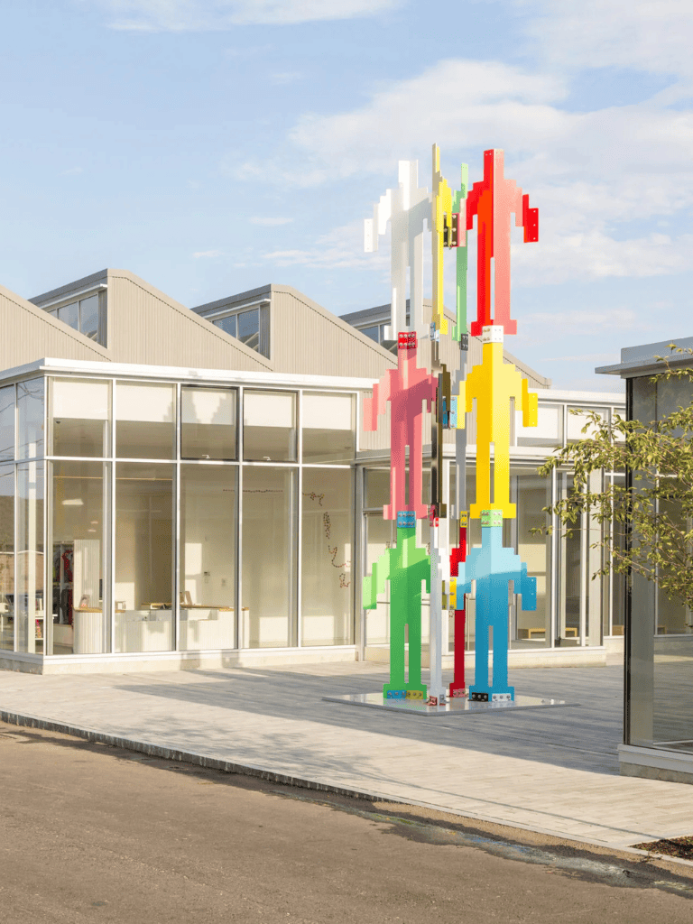 Colorful LEGO-inspired human sculpture outside modern building in daytime.