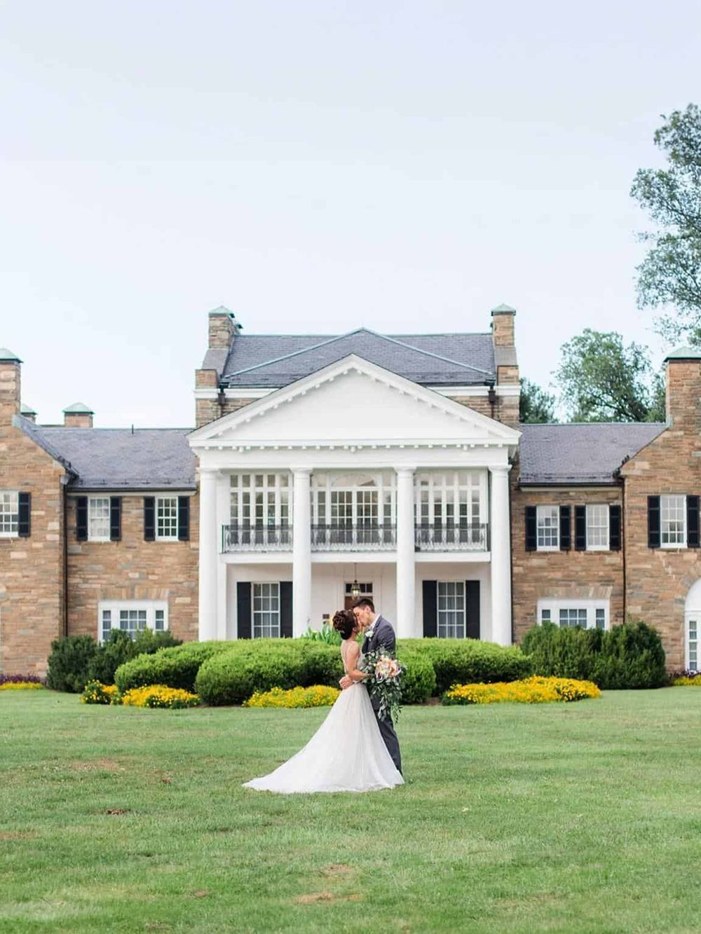 Elegant couple kissing in front of a historic mansion, ideal for wedding photography and special events.