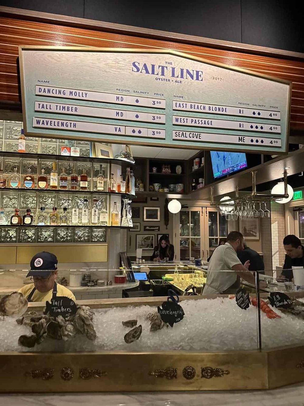 Fresh oysters and seafood at a bar with a digital menu displaying regional oyster varieties and prices.