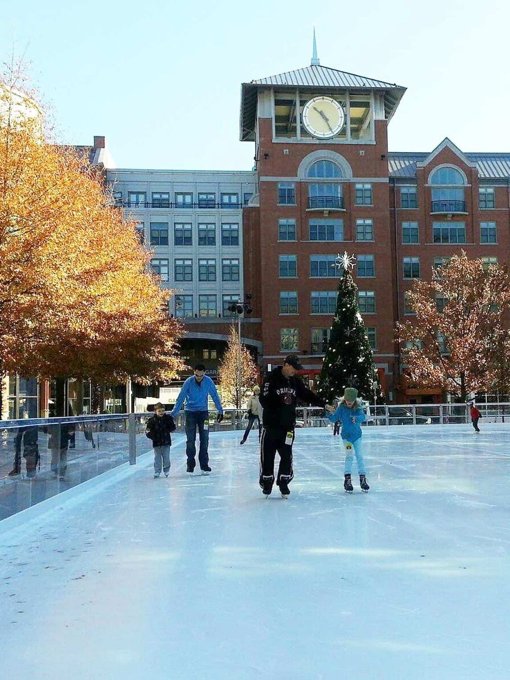 Ice skating in outdoor rink during winter, with festive Christmas tree and historic building in background.