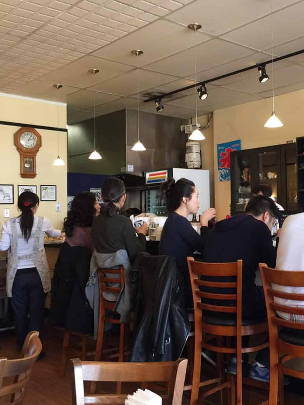 Cozy Japanese restaurant interior with customers dining and staff serving in a warm setting.