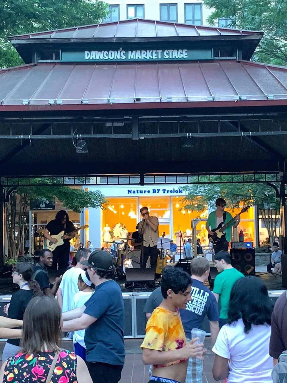 Vibrant outdoor concert at Dawson's Market Stage with live band and audience enjoying music and drinks.