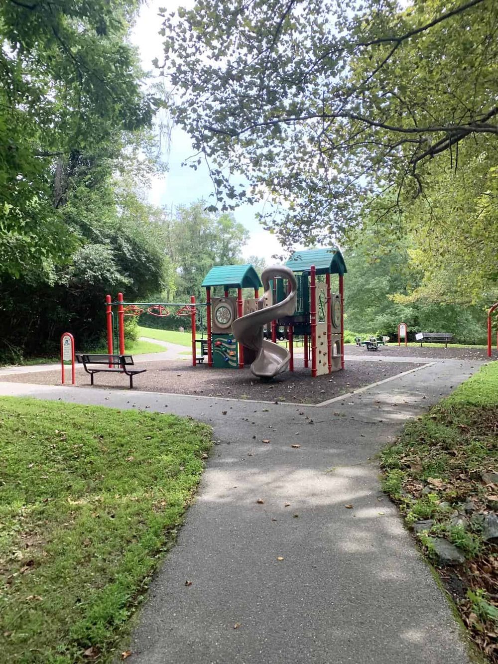 Colorful children's playground in a lush park with trees and walking trails.