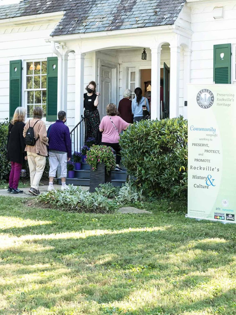 People gathering outside historic house for community event, preserving Rockville's heritage.