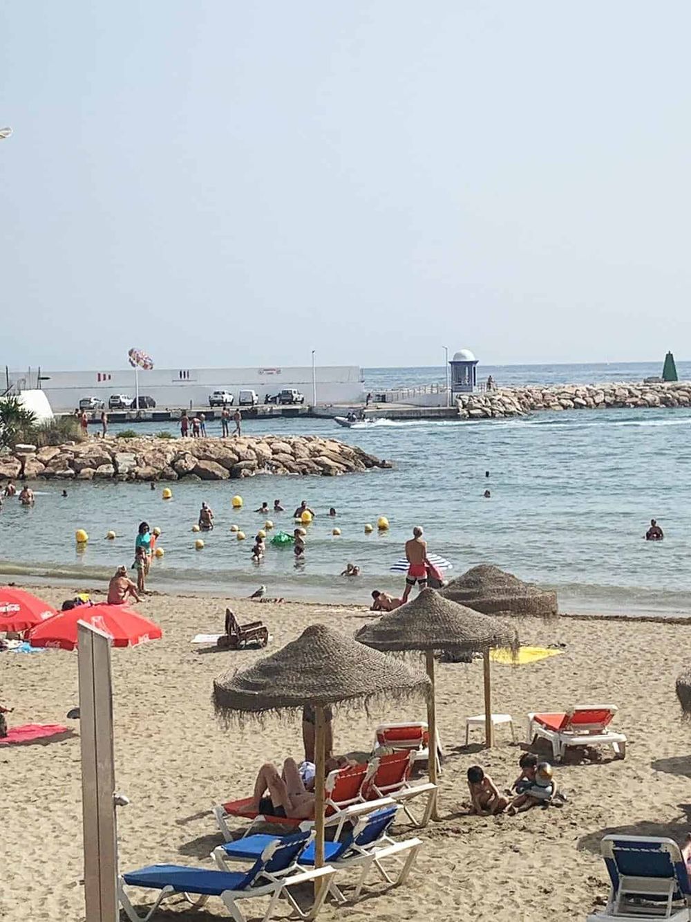 Sunset Beach with umbrellas, lounge chairs, and people swimming in the ocean, capturing a relaxing seaside experience.