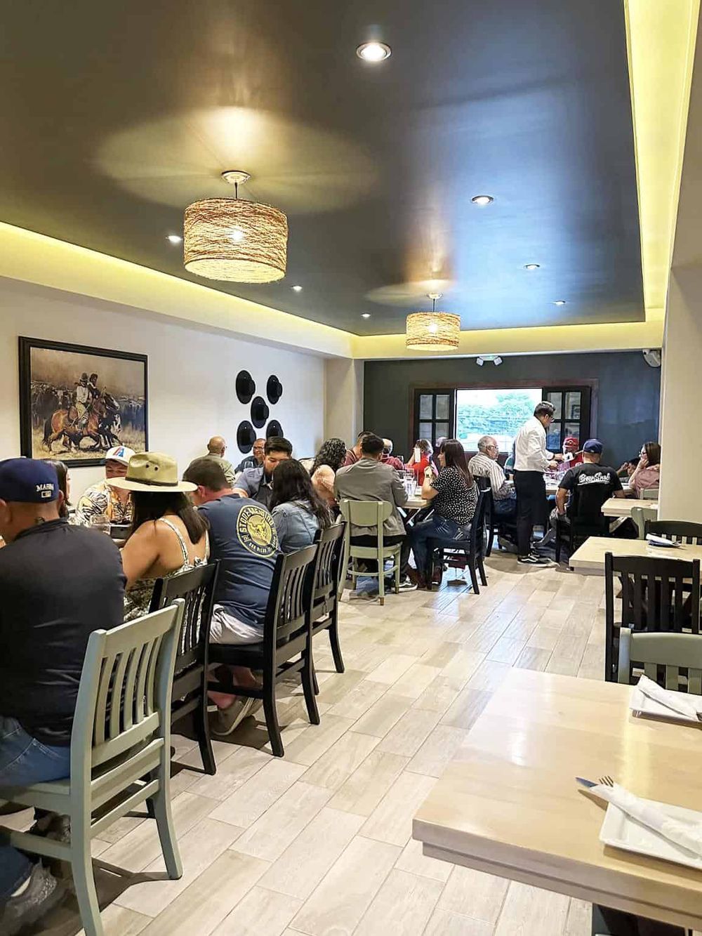 Busy restaurant interior with diverse guests dining and a chef serving at the table.