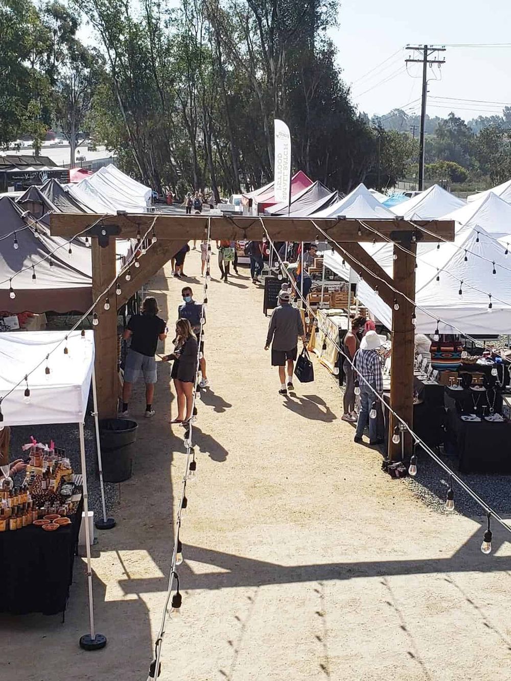 Colorful outdoor marketplace with white tents, shoppers, and vendor booths at QuestForDirections event.