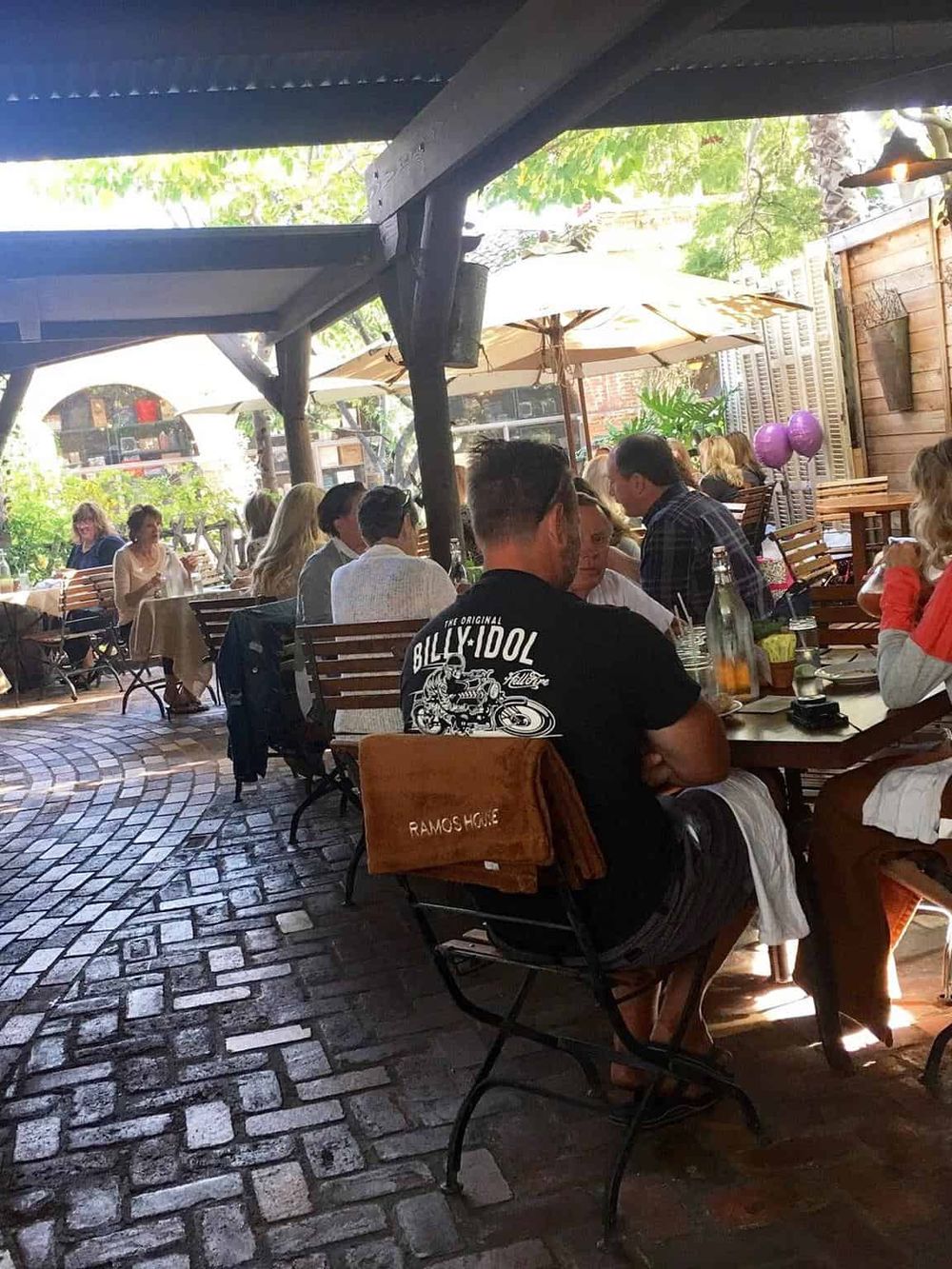 Outdoor dining at a cozy restaurant with wooden furniture, umbrellas, and lush greenery.