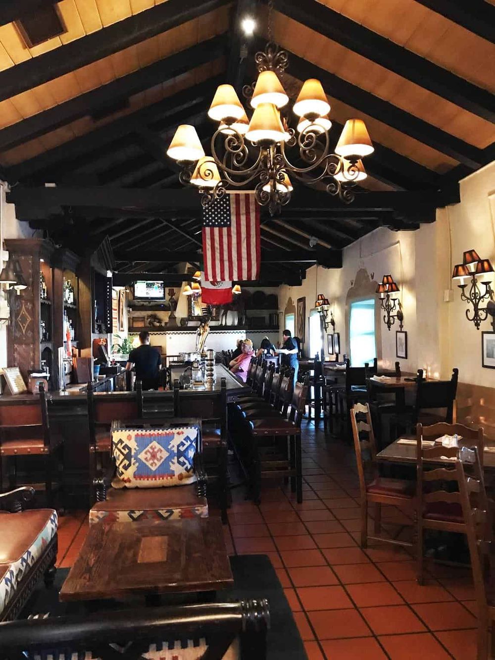 Cozy restaurant interior with wooden beams, elegant chandelier, and American flag, perfect for dining and social gatherings.