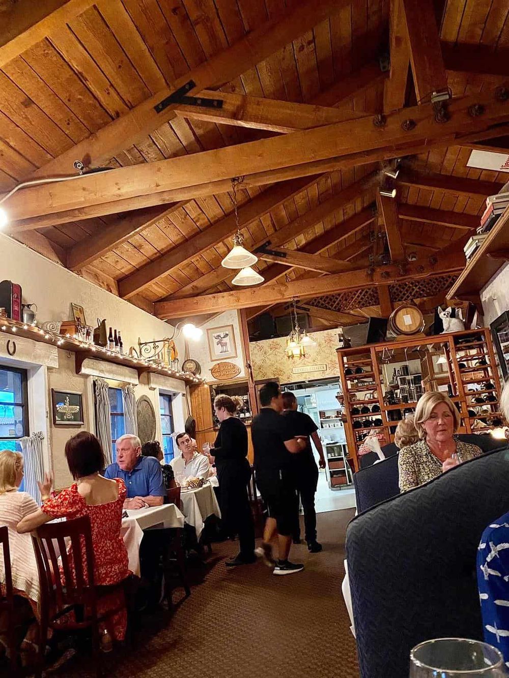 Cozy restaurant interior with wooden beams, warm lighting, and patrons dining.