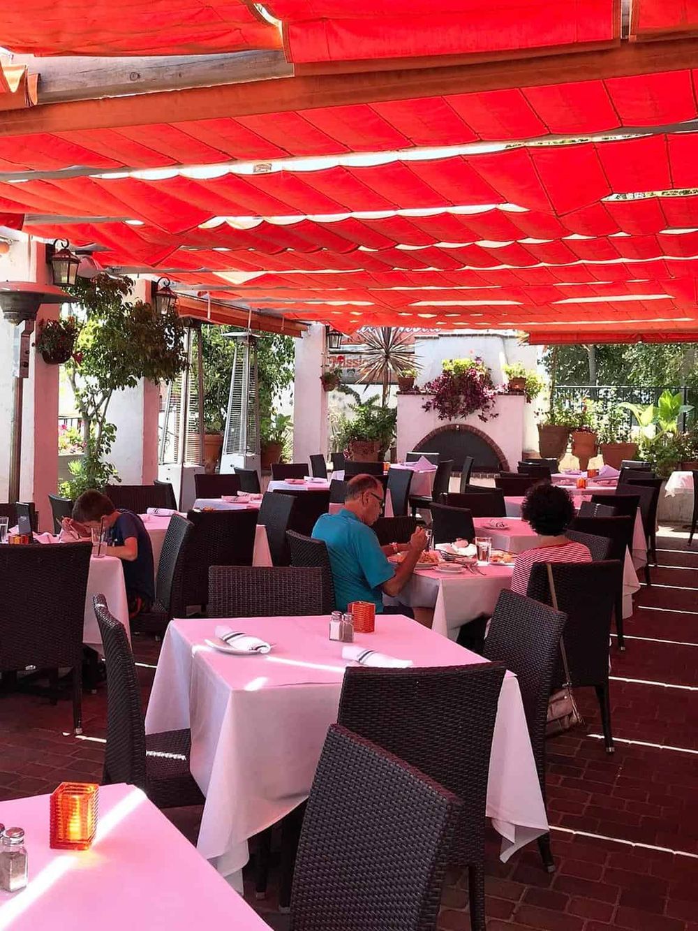 Al fresco dining restaurant patio with red canopy and potted plants, family-friendly environment, perfect for outdoor meals.