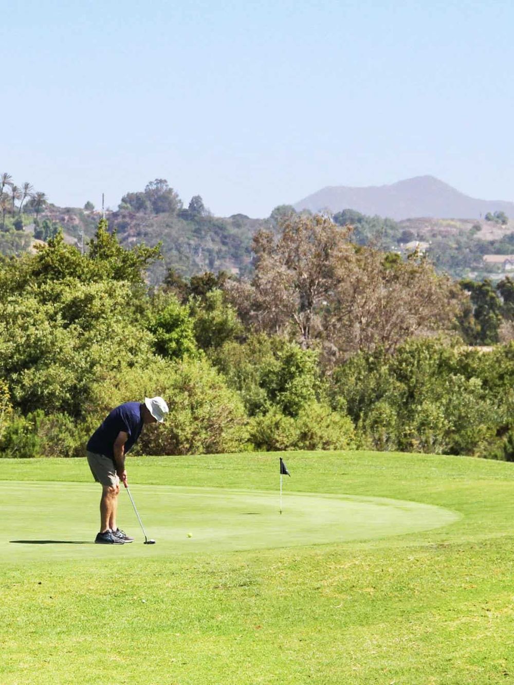 Beautiful golf course landscape with player preparing to putt, scenic hills in background.