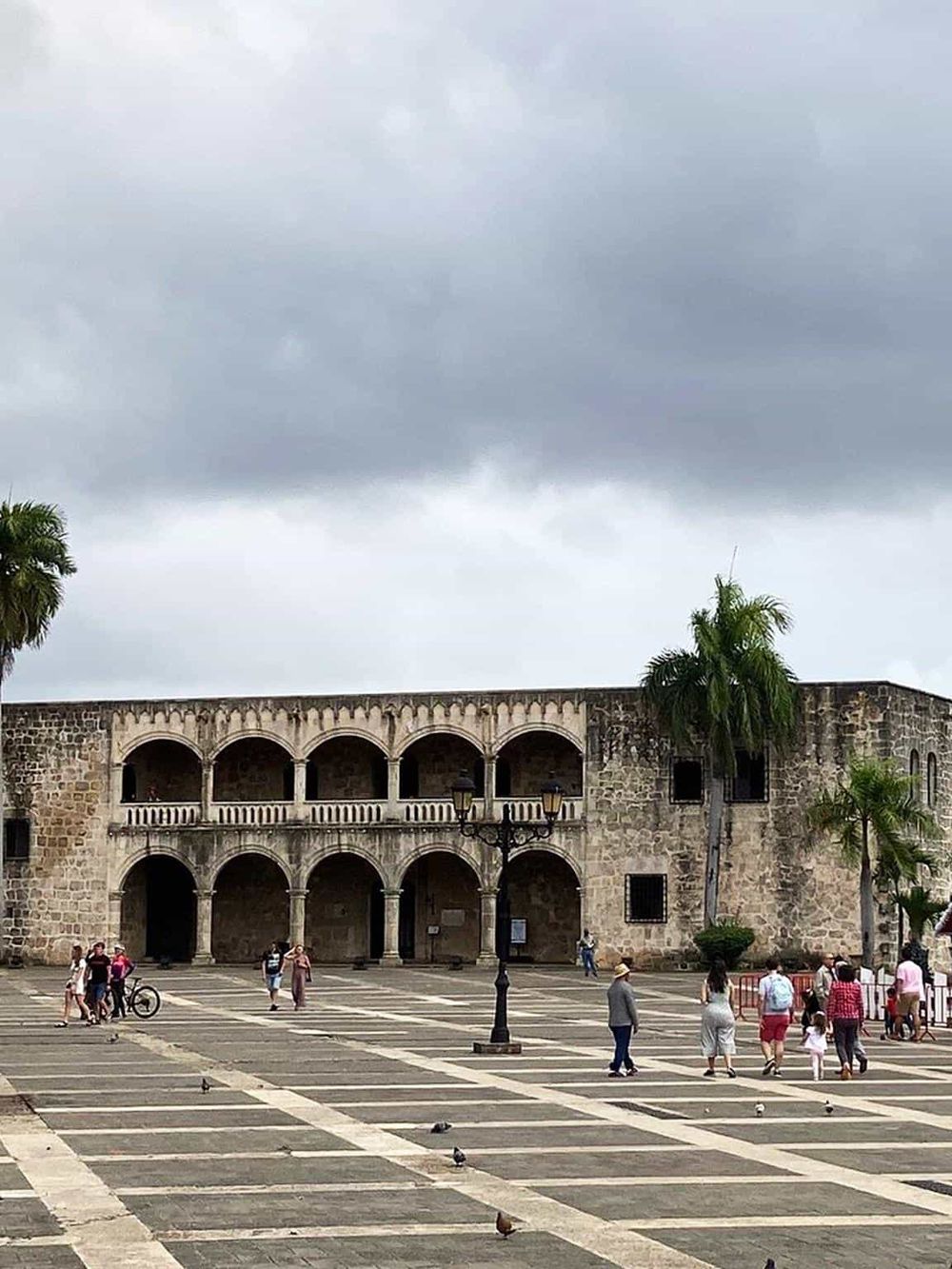 Ancient stone fortress with arches, palm trees, and visitors in a historic city square, showcasing Mexico's rich architectural heritage.