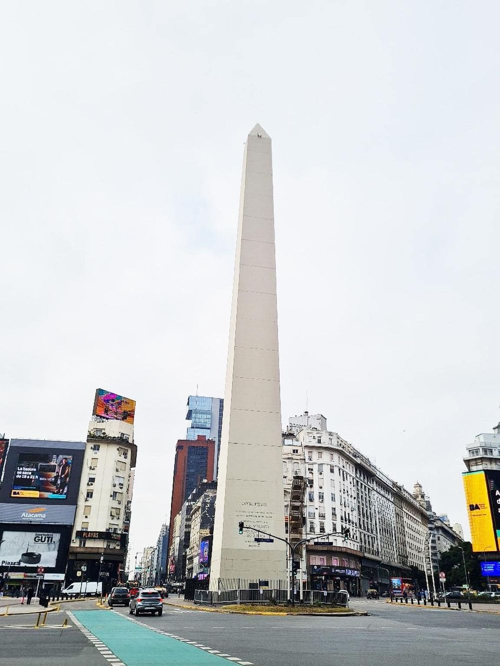 1. Tall urban obelisk standing in city center with surrounding buildings and digital billboards.