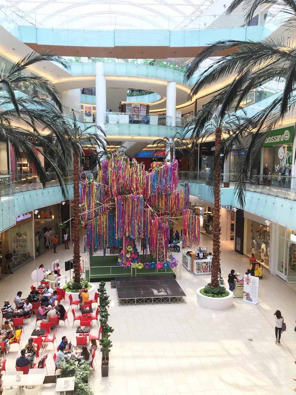 Colorful art installation at a modern shopping mall with palm trees and seating areas.