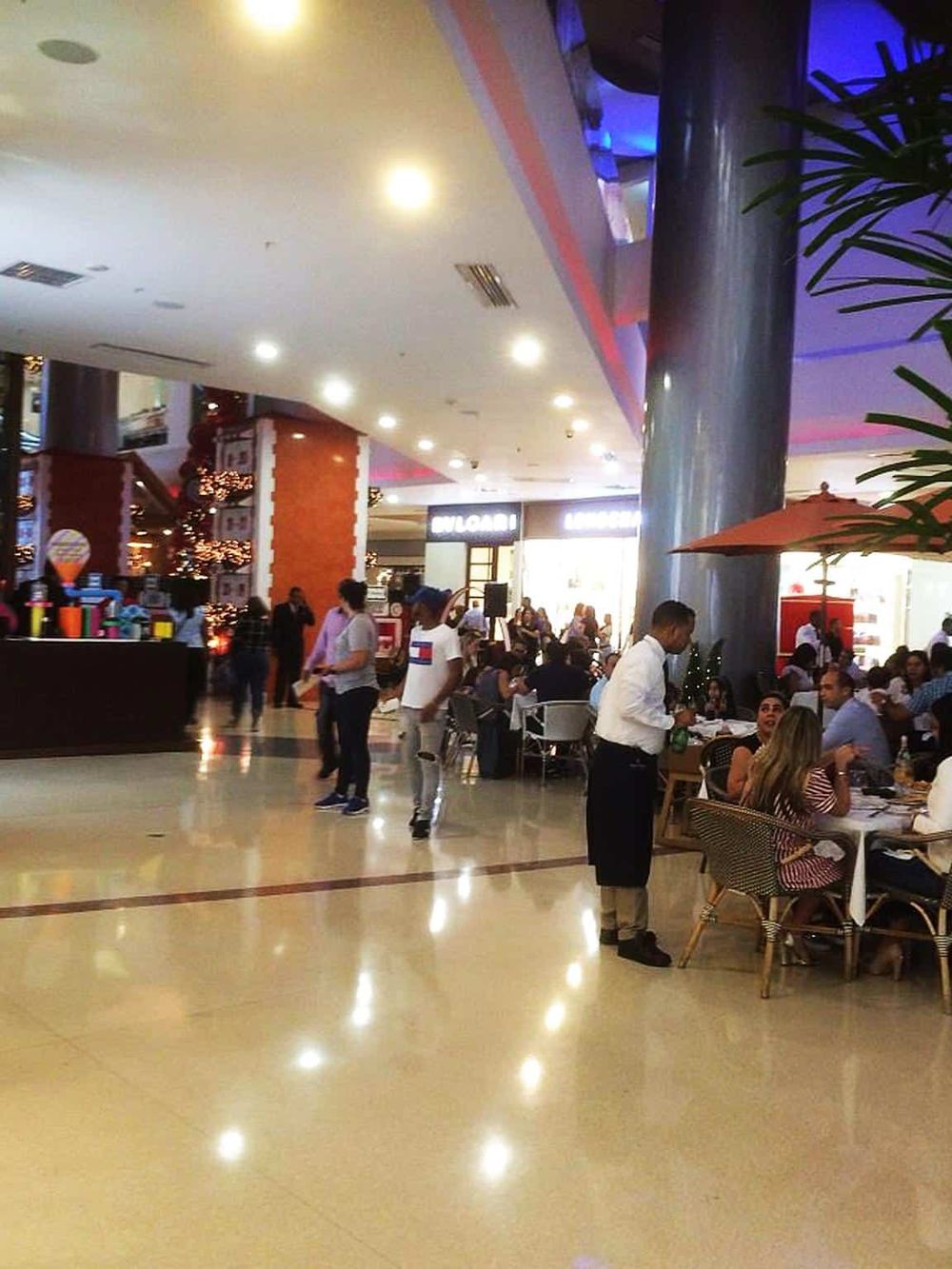 Bright indoor mall food court bustling with shoppers and diners enjoying diverse dining options.