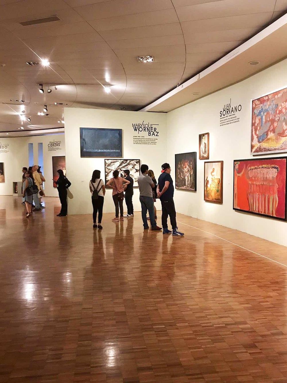 Colorful art gallery inside a museum with visitors viewing paintings and exhibits.