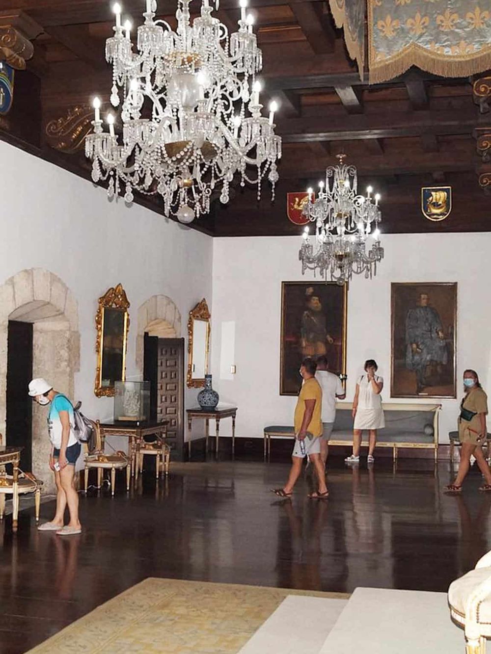 Luxurious chandelier in historic castle interior with visitors and ornate decor, showcasing elegance and grandeur.