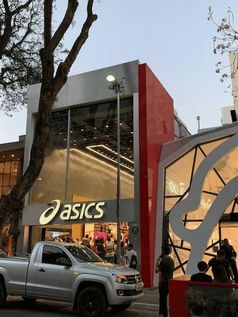 Modern ASICS store exterior with glass facade and busy shoppers, urban retail shopping experience.