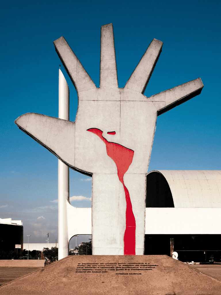 A hand-shaped monument with a map of Israel painted on it, under a clear blue sky, symbolizing guidance and navigation.