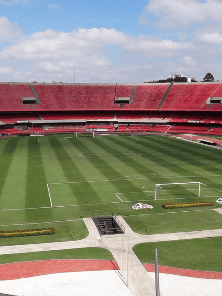 Spacious soccer stadium with lush green field and red seating area.