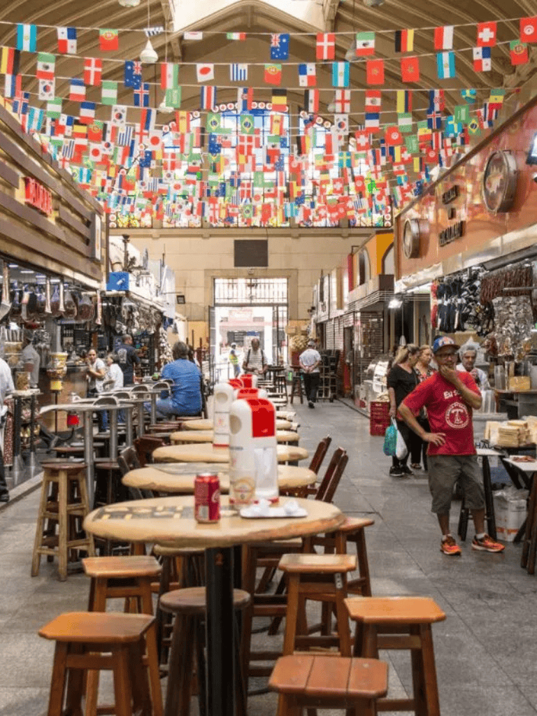 Flags of various countries hanging from the ceiling in a lively marketplace or food hall.