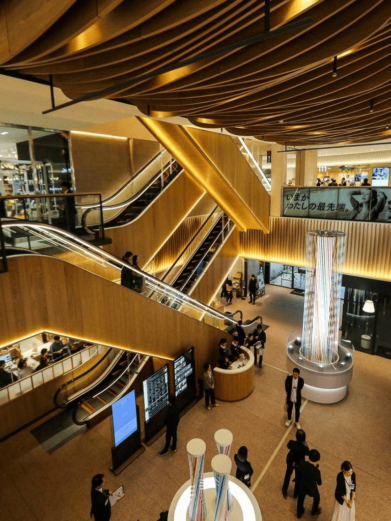 Modern shopping mall interior with escalators, digital kiosks, and decorative lighting features.