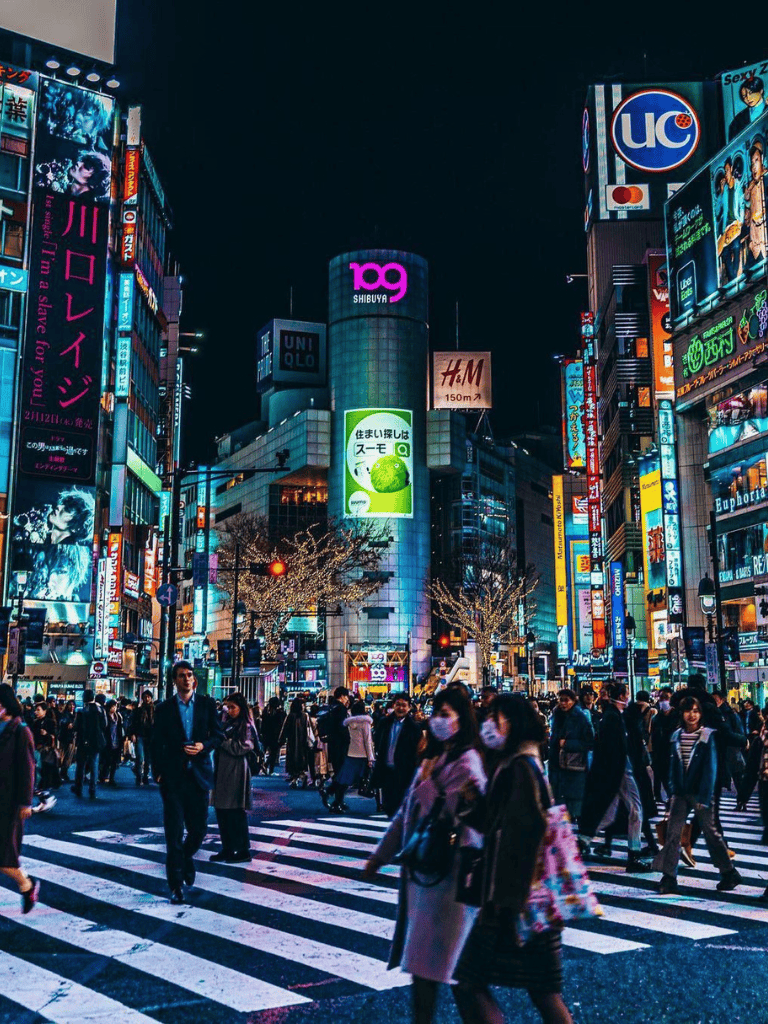 Bright Tokyo cityscape at night with illuminated billboards and busy crosswalk filled with pedestrians.