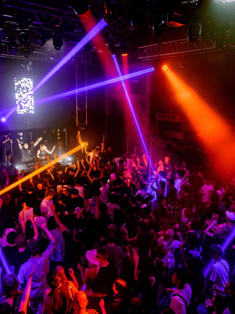 Dance club with vibrant lighting, DJ, and energetic crowd at night event.