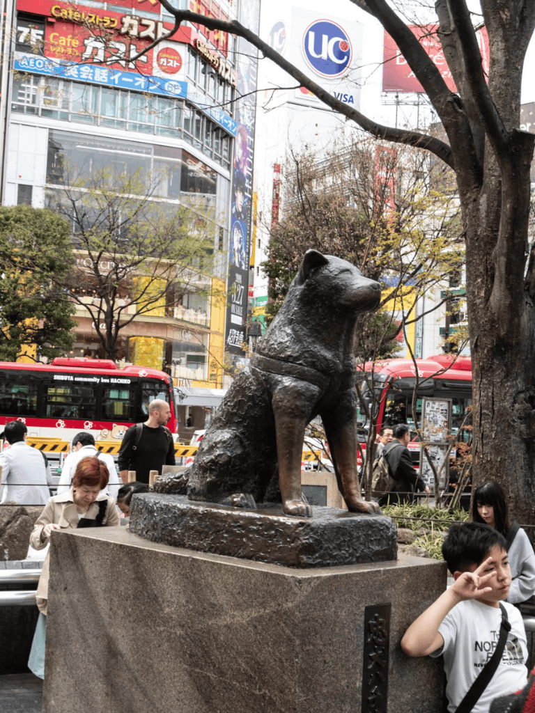 Small dog statue in iconic urban setting with crowded streets and vibrant advertisements.