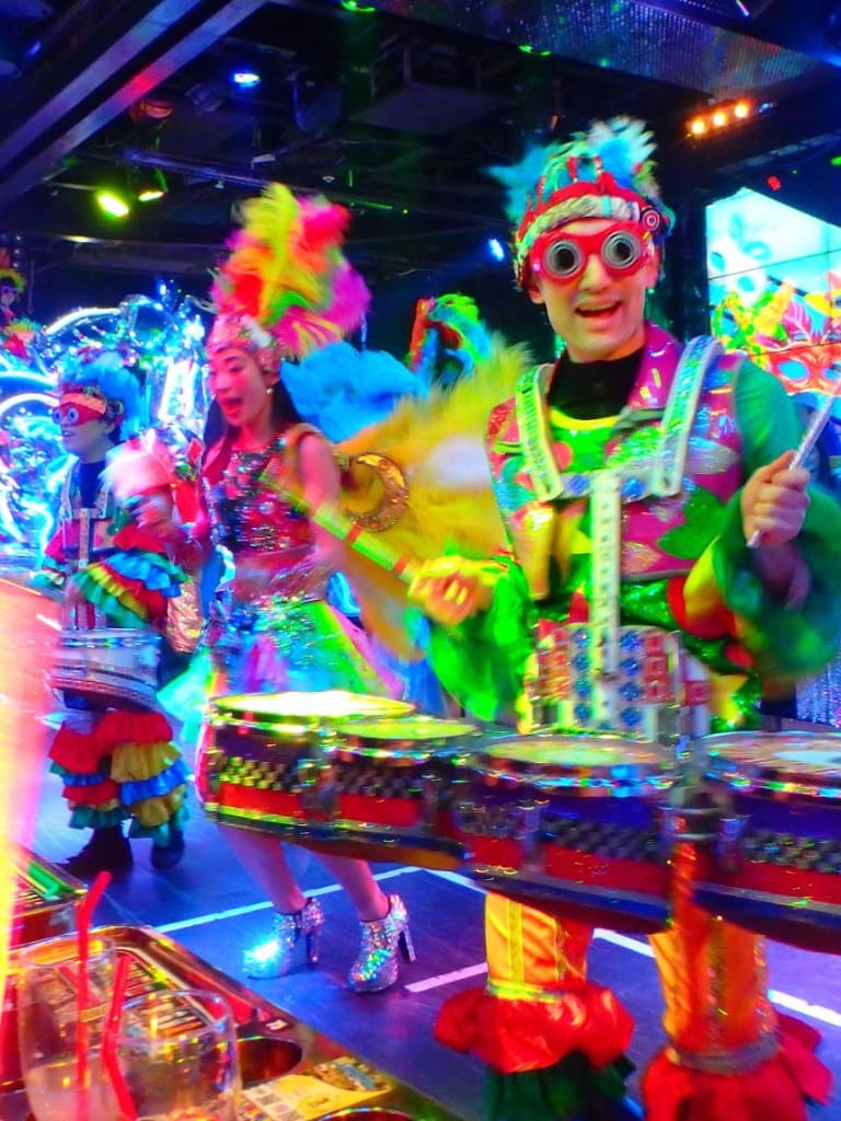 Colorful carnival performers dancing in neon costumes and bright feathers at QuestForDirections.