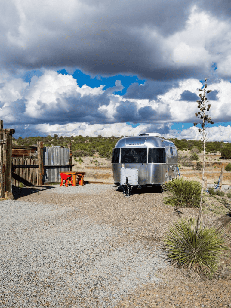 Airstream trailer in desert landscape with cloudy sky, rugged outdoor setting, and minimal desert vegetation.