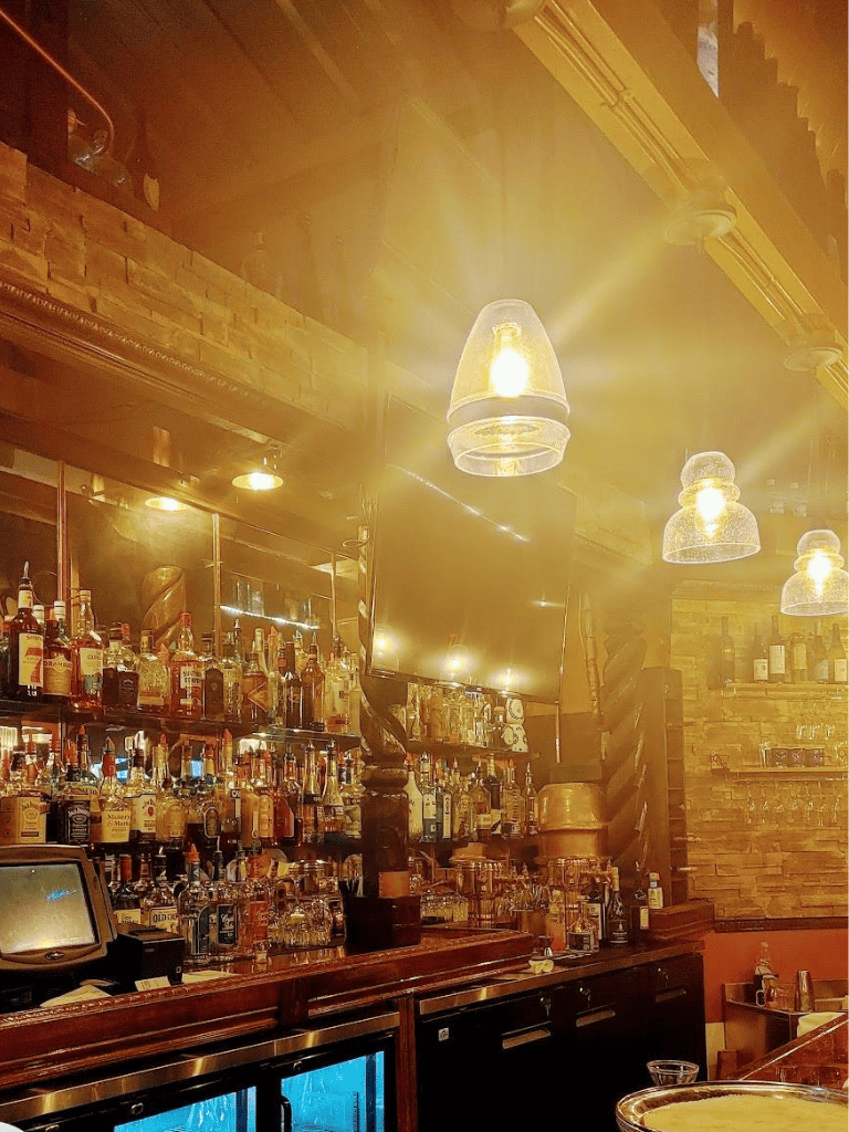 Brightly lit bar with various liquor bottles and warm ambient lighting, perfect for a cozy night out.