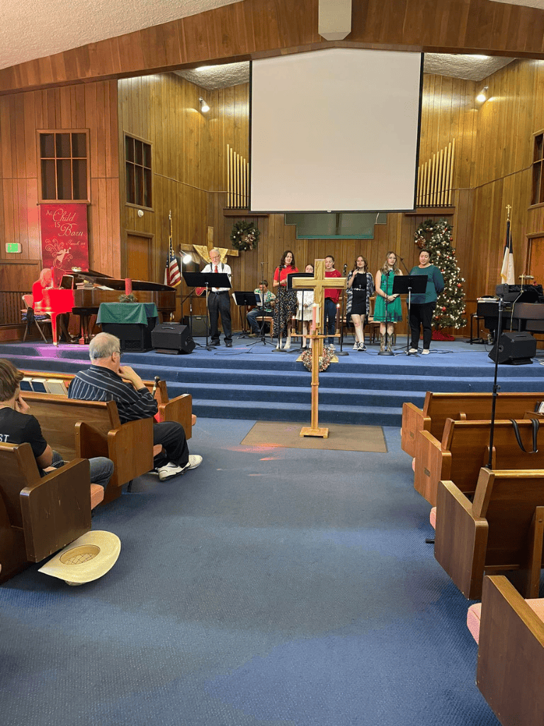 Christmas choir performance at church with decorated trees and choir members singing on stage.