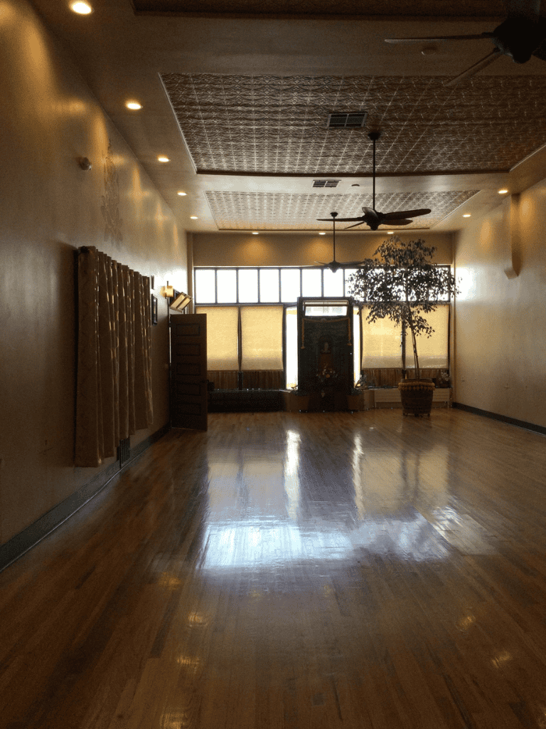 Spacious indoor room with hardwood floors, ceiling fan, and large window with curtains.