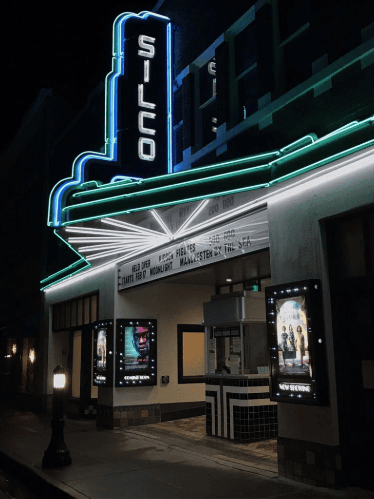 Neon Silos Theater marquee at night, showcasing movie posters and vibrant signage for local cinema.