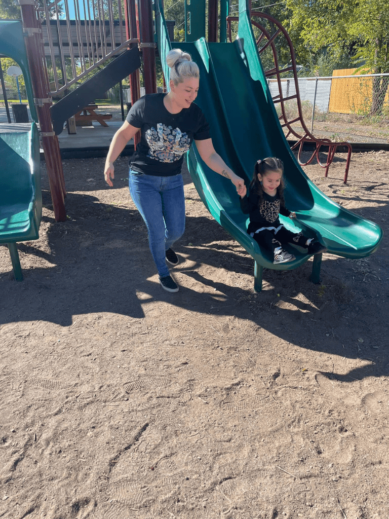 Child sliding down playground slide with adult at QuestForDirections park.