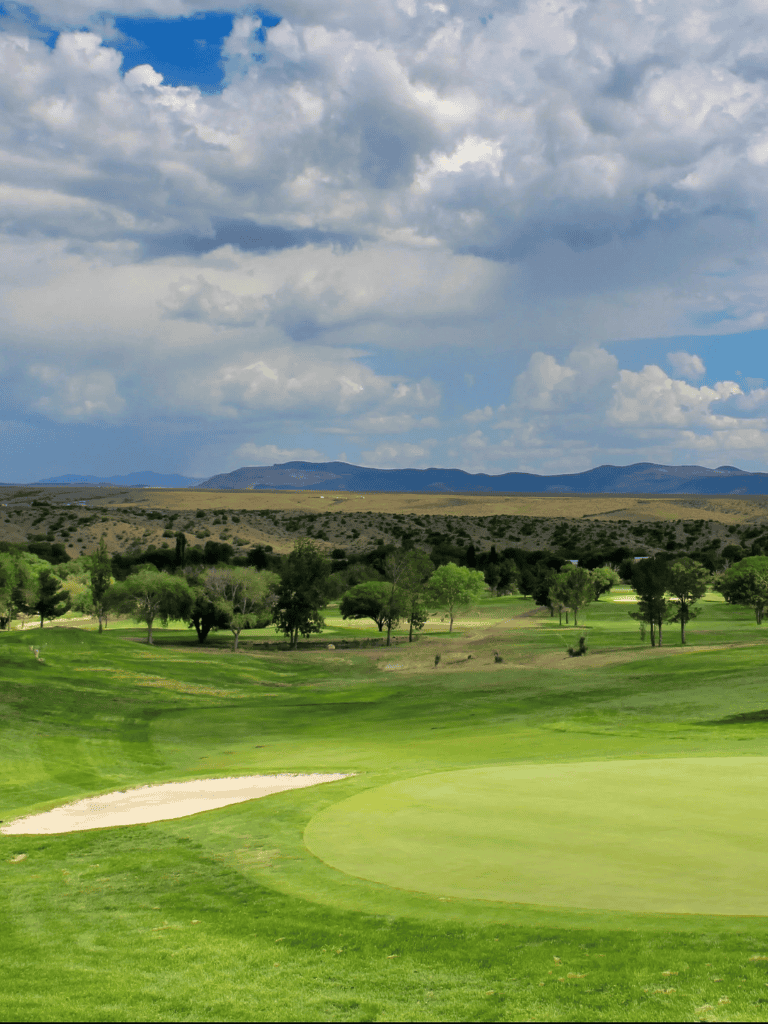 Lush golf course with green fairways and sand bunkers under a cloudy sky.