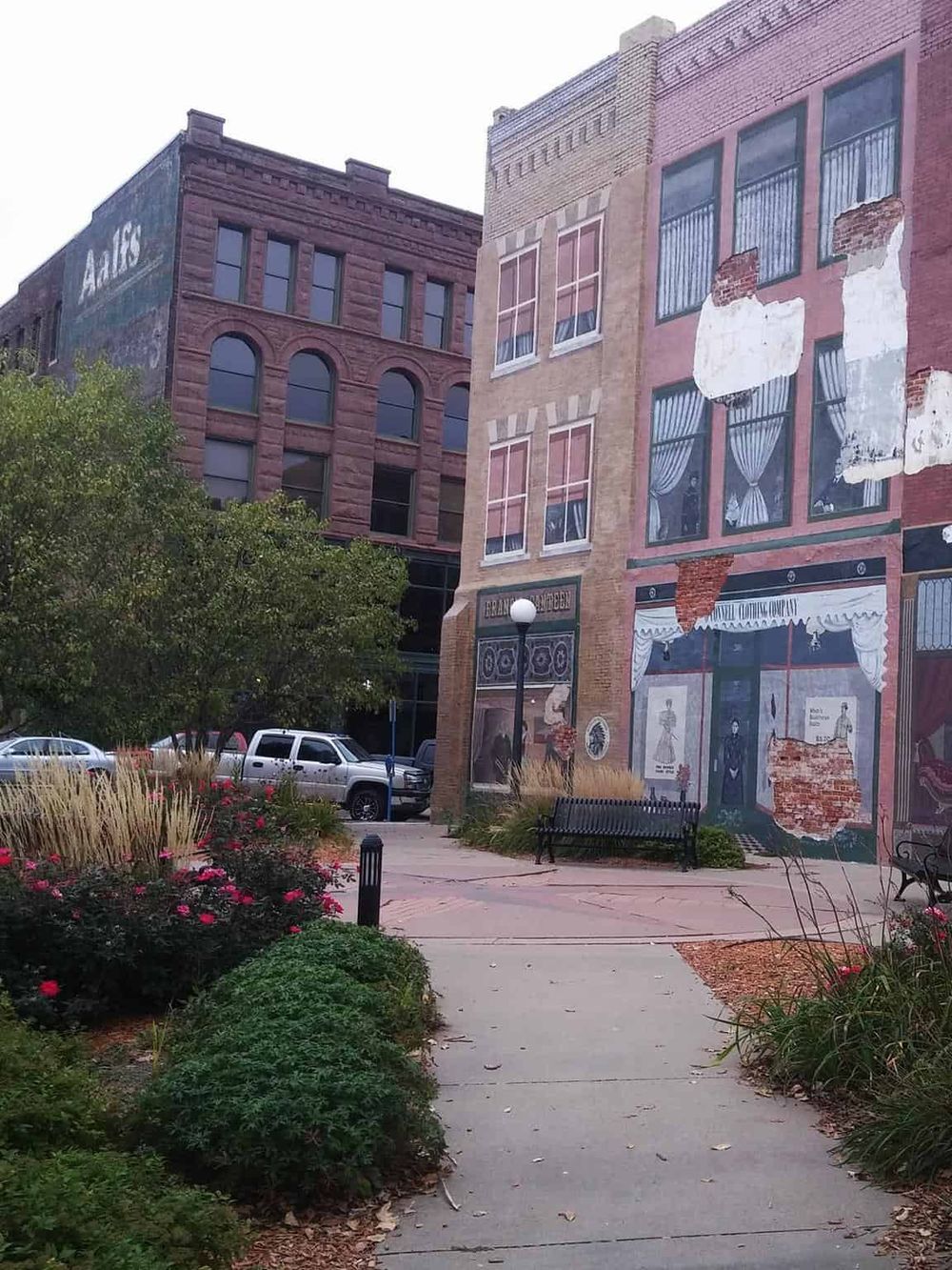 Colorful historic downtown street with mural and brick buildings, local shops, and a peaceful park setting.