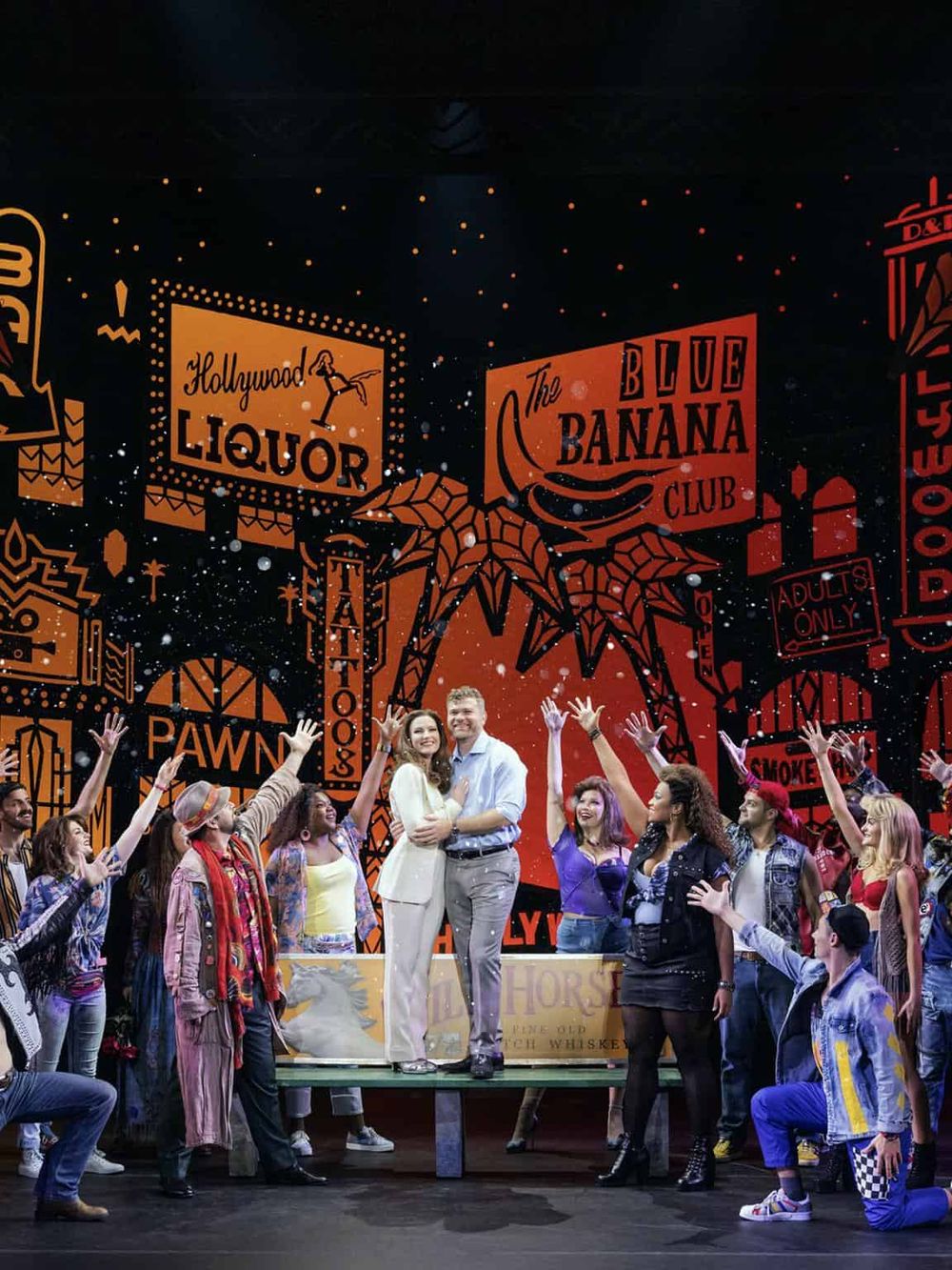 Colorful stage performance with diverse cast, vibrant signs, and lively audience at QuestForDirections event.