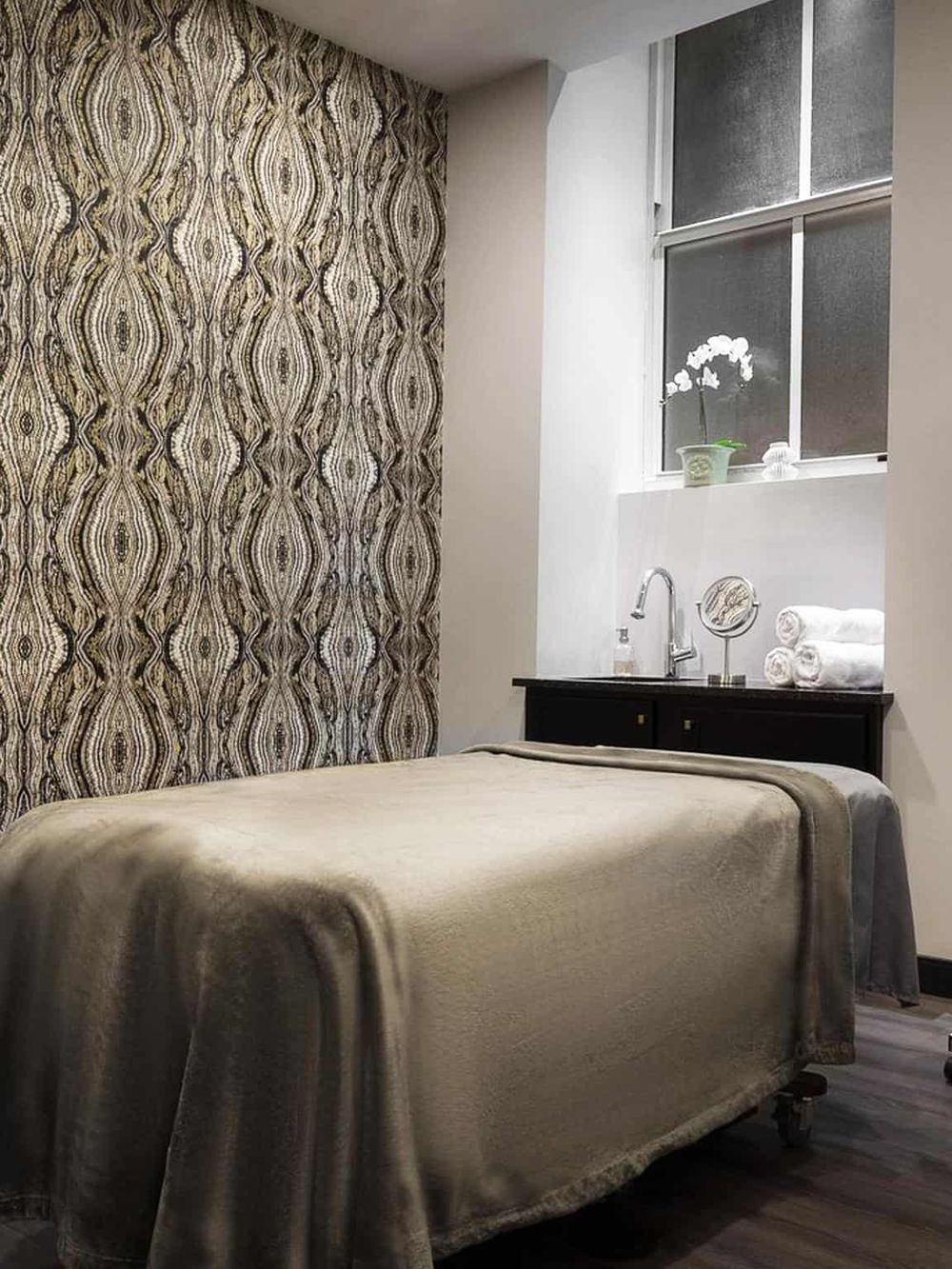 Relaxing massage room with spa bed, elegant decor, and natural light from window, perfect for wellness treatments.