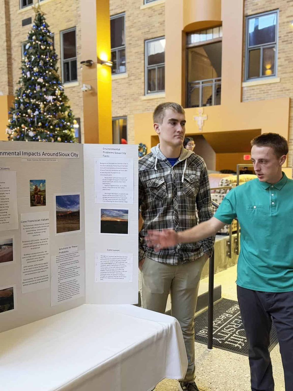 Young men presenting a research project at Sioux City event, showcasing environmental impacts, solutions, and conservation efforts.
